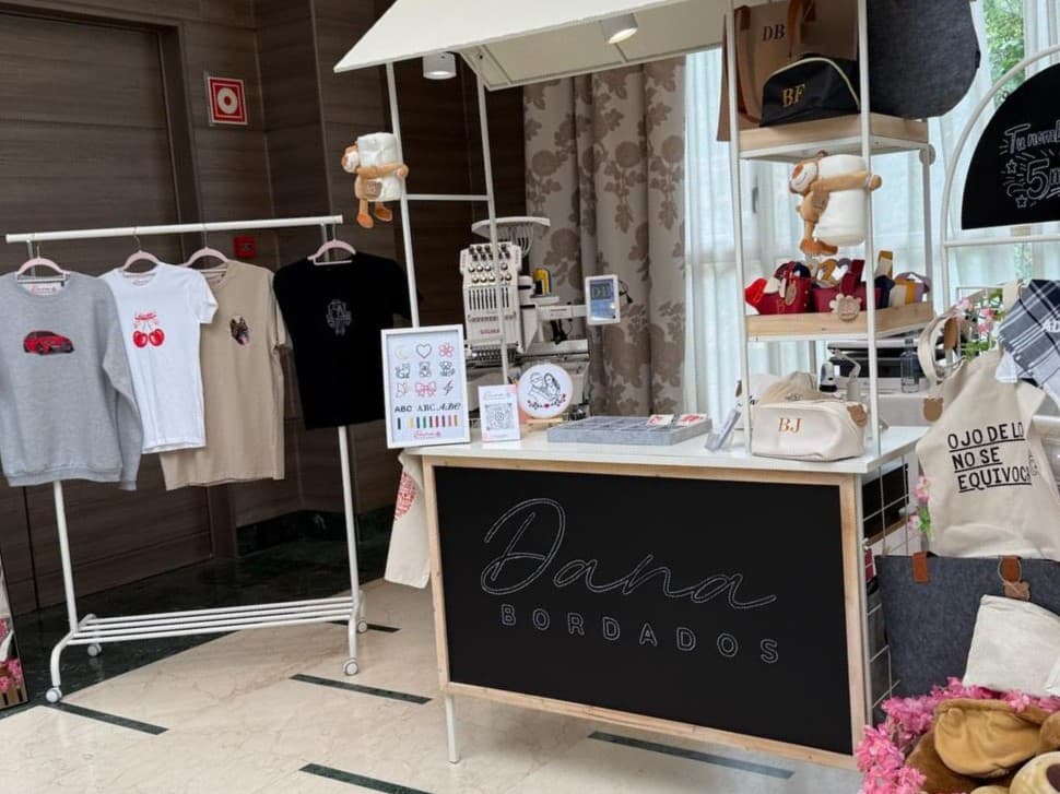 Stand de DANA Bordados en un evento, con máquina de bordar, prendas y productos personalizados